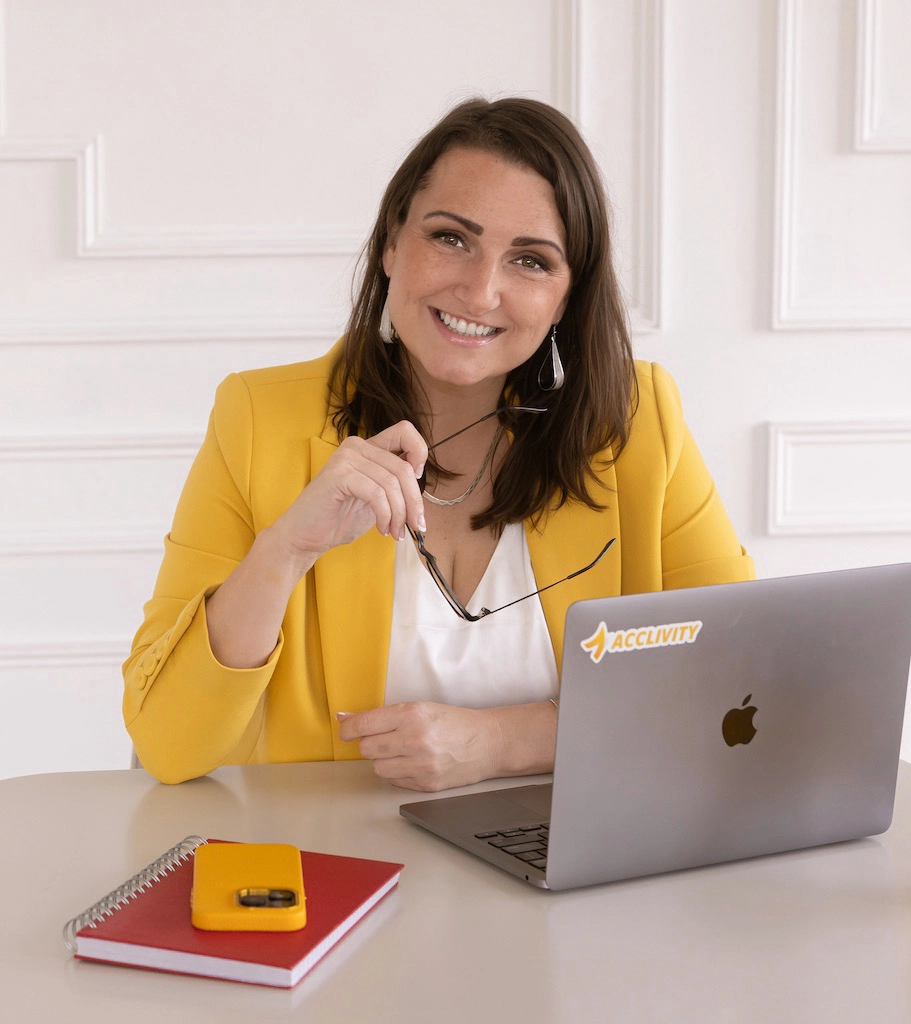 Shawna Tregunna wearing a yellow blazer is seated at a desk, focused on her laptop, exuding professionalism and confidence.