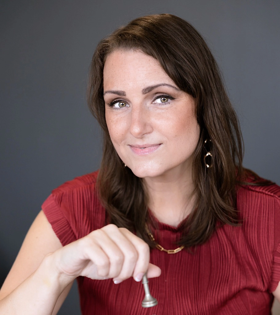 Shawna Tregunna wearing a red shirt is holding a shiny silver key in her hand, showcasing a moment of anticipation or discovery.